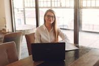 Confident businesswoman working remotely with a laptop by the window in a bright, modern office.